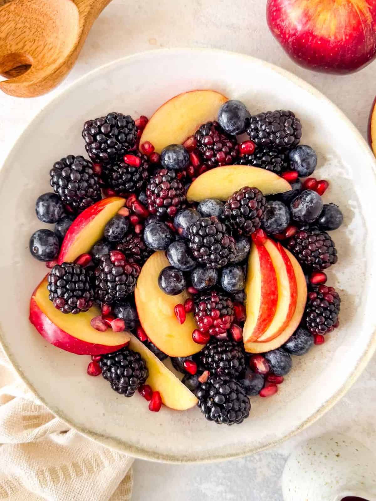 fall fruit salad with apples, blackberries, blueberries and pomegranate seeds in a bowl.