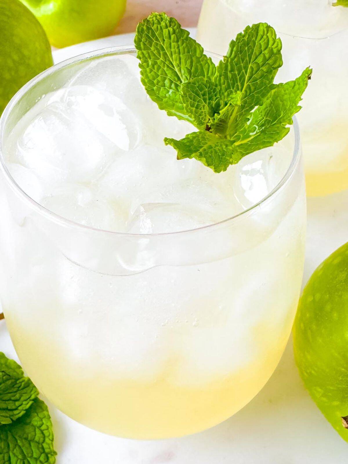 green apple mocktail in a glass next to green apples.