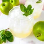 green apple mocktails in two glasses next to Granny Smith apples and mint leaves.