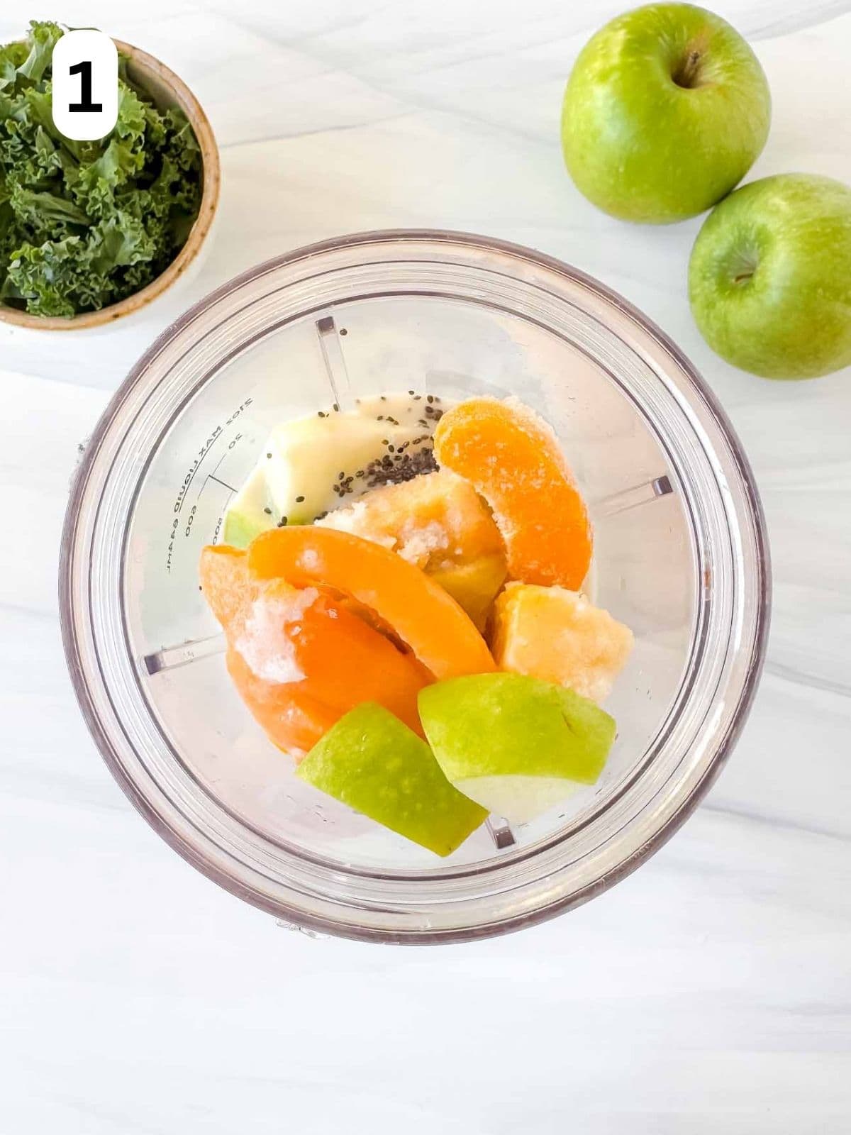diced apple, kale, chia seeds, plant milk and frozen peaches in a blender cup labelled number one.