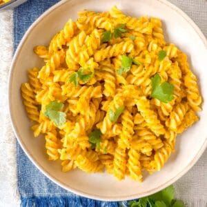 roasted carrot pasta in a bowl garnished with fresh parsley on a blue cloth.