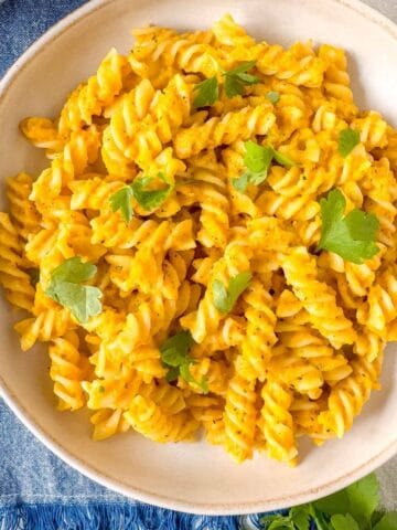 roasted carrot pasta in a bowl garnished with fresh parsley on a blue cloth.