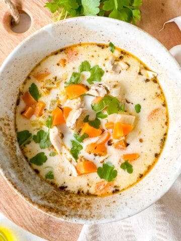 dairy free creamy chicken soup in a bowl next to fresh parsley and garlic cloves.