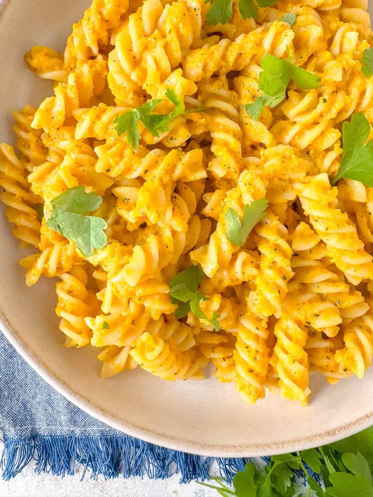 carrot pasta in a bowl garnished with fresh parsley on a blue cloth.