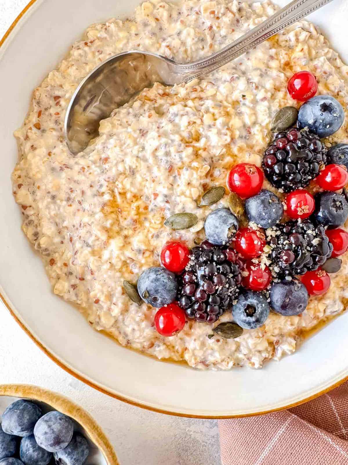 flaxseed overnight oats in a white bowl topped with fruit and maple syrup.