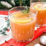 mulled apple juice in a glass garnished with an apple slice and cloves on a festive cloth.