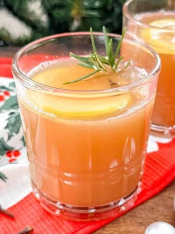 mulled apple juice in a glass garnished with an apple slice and cloves on a festive cloth.