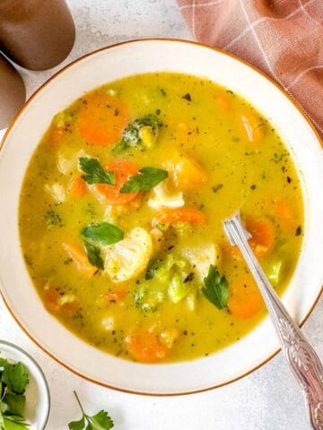 frozen vegetable soup in a white bowl next to fresh parsley and a brown cloth.