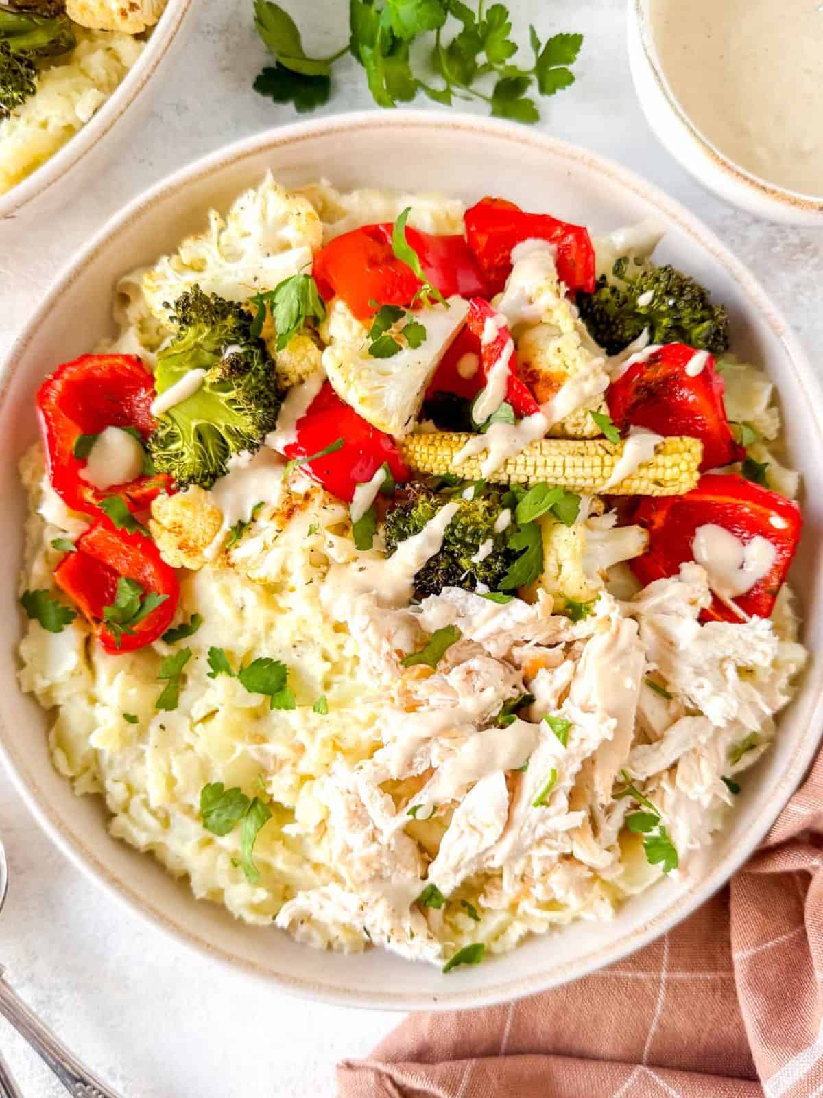 loaded chicken mashed potato bowls next to a bowl of tahini and fresh herbs.