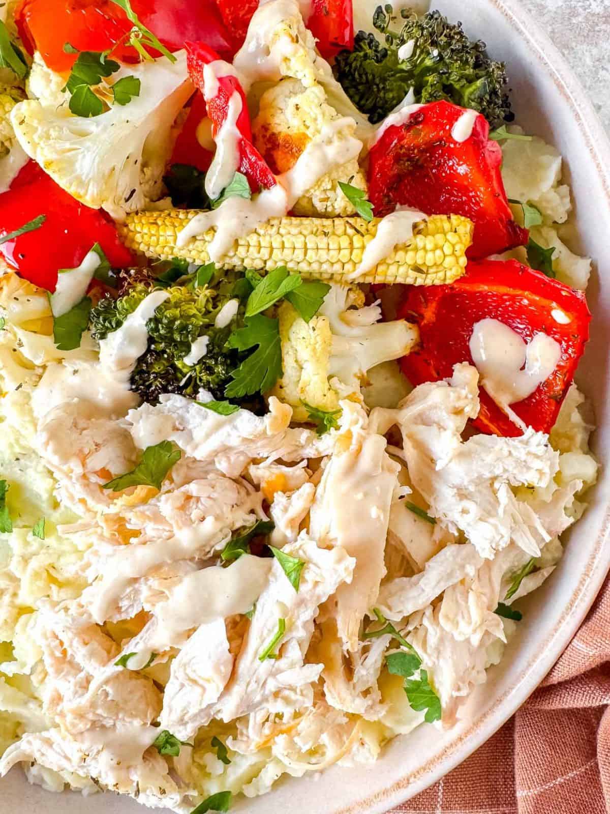 mashed potato bowl with chicken and vegetables drizzled with tahini dressing.