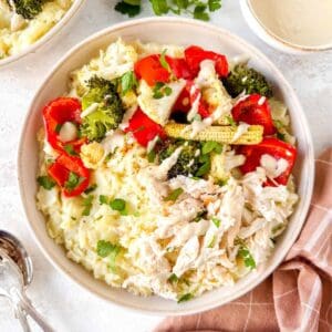 mashed potato bowls with chicken and vegetables drizzled with tahini dressing next to fresh herbs and a brown cloth.