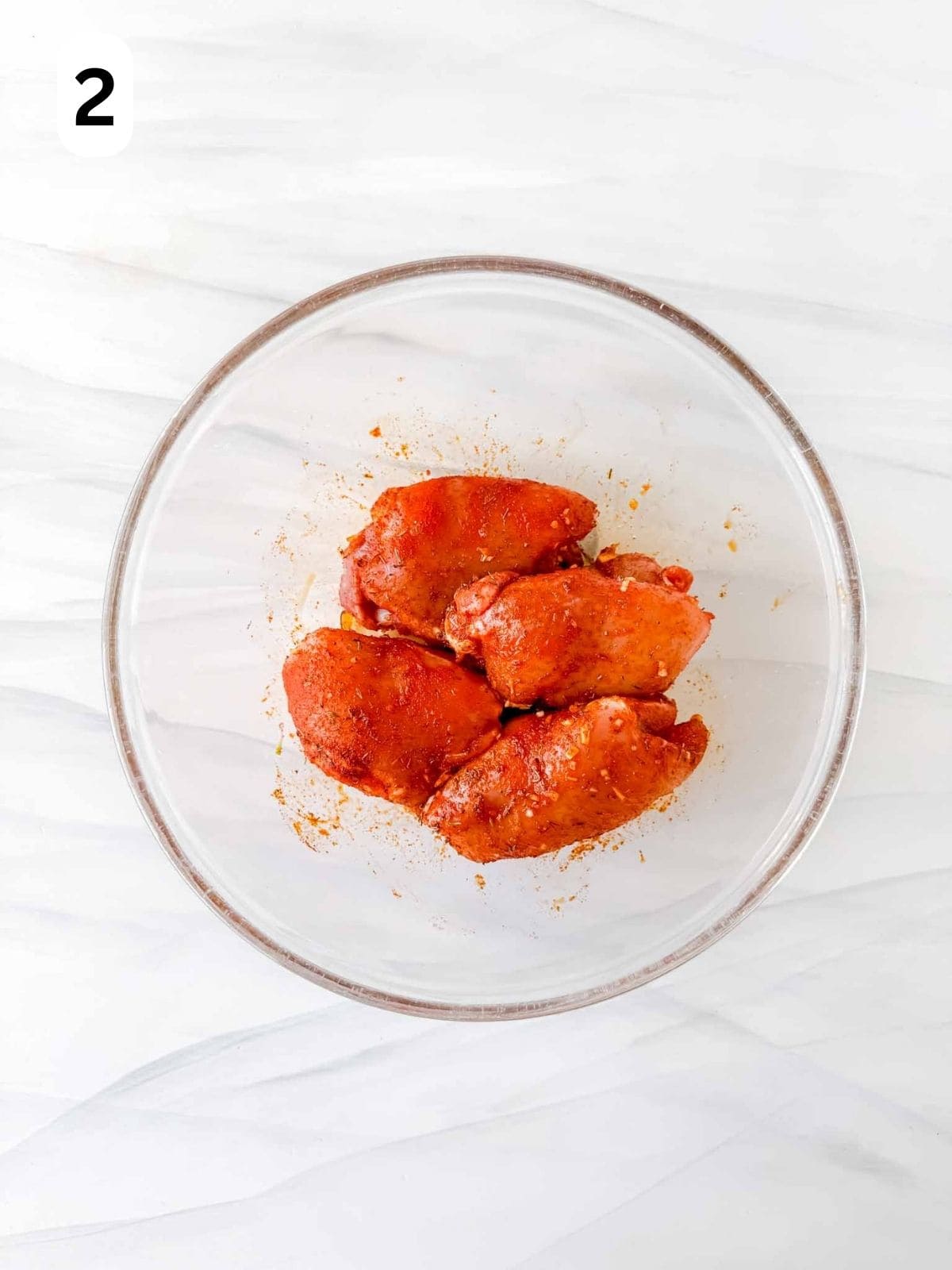 chicken thighs coated with paprika and spices in a glass bowl labelled number two.
