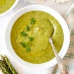 asparagus potato soup in a white bowl next to a bunch of asparagus.