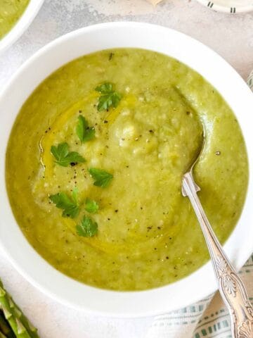 asparagus potato soup in a white bowl next to a bunch of asparagus.