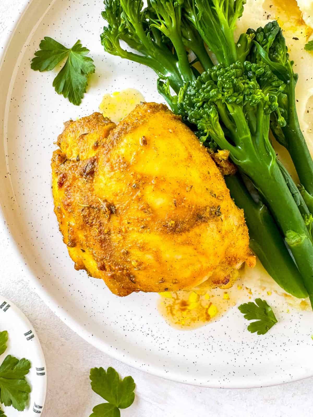 cardamom chicken on a plate with broccoli and mashed potatoes.
