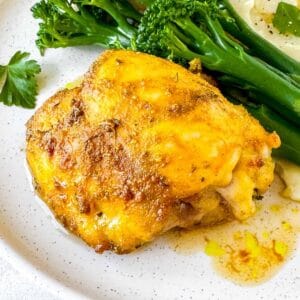cardamom chicken thigh on a plate with broccoli and mashed potatoes.
