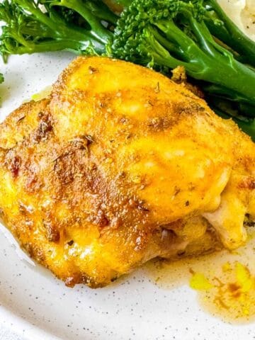 cardamom chicken thigh on a plate with broccoli and mashed potatoes.