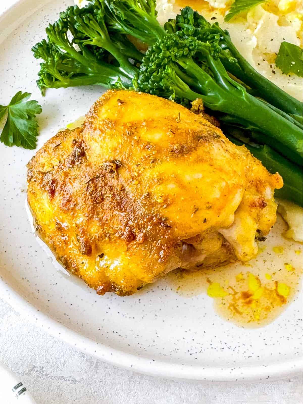 cardamom chicken thigh on a plate with broccoli and mashed potatoes.