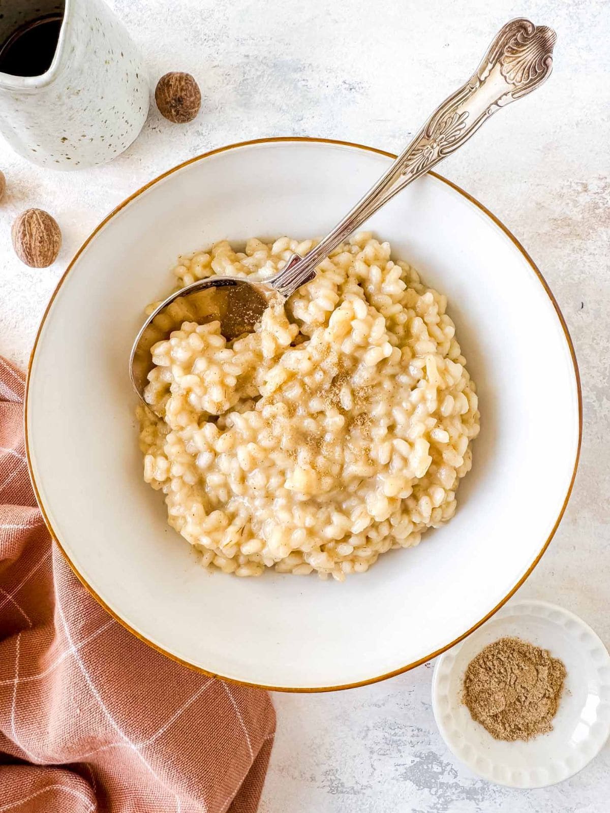 cardamom rice pudding in a white bowl next to a small jug and small bowl of ground cardamom.