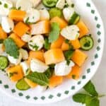cantaloupe salad with mozzarella, cucumber and mint leaves on a white plate.