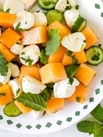 cantaloupe salad with mozzarella, cucumber and mint leaves on a white plate.
