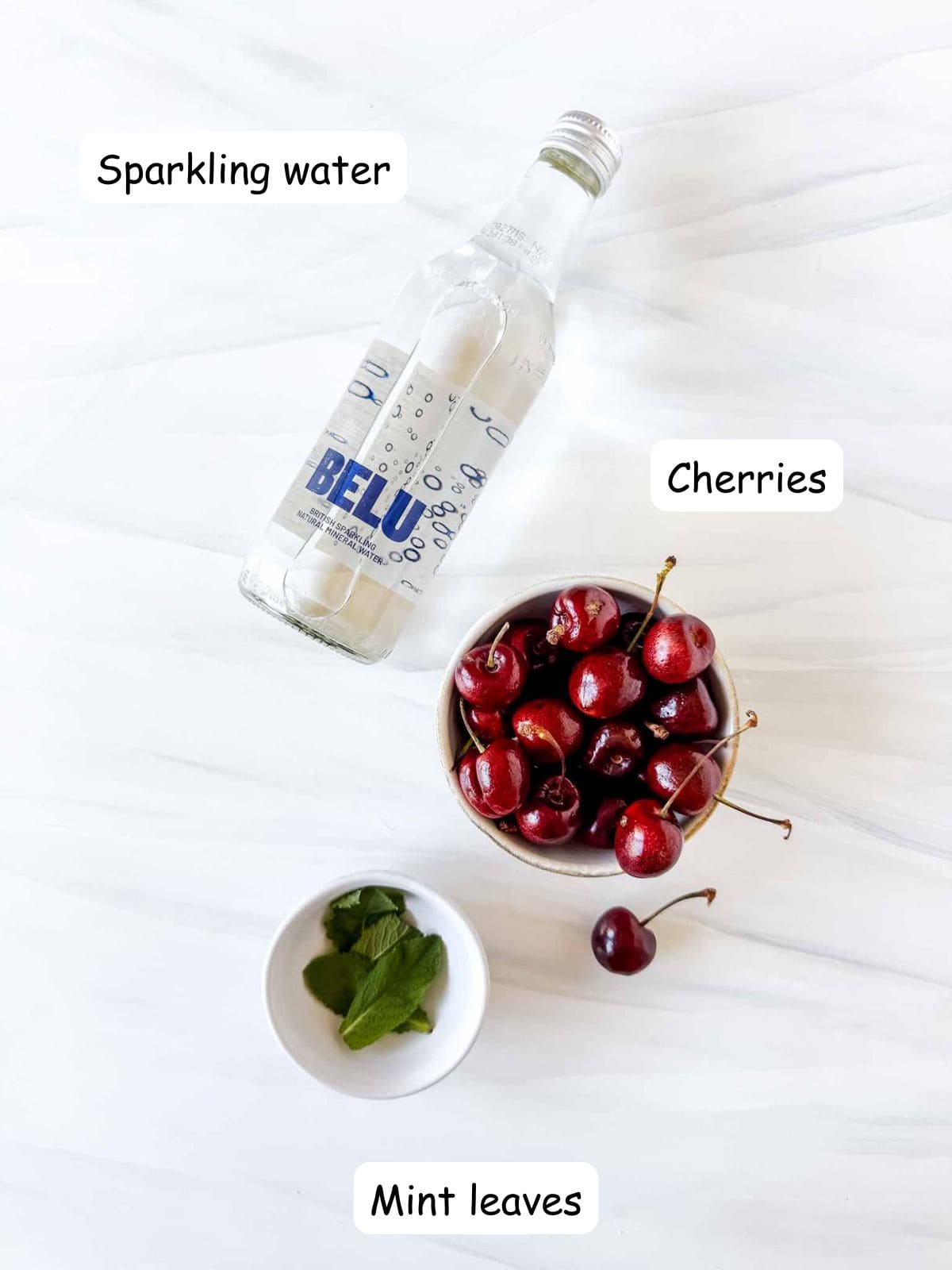 individually labelled bottle of sparkling water, cherries and mint leaves.
