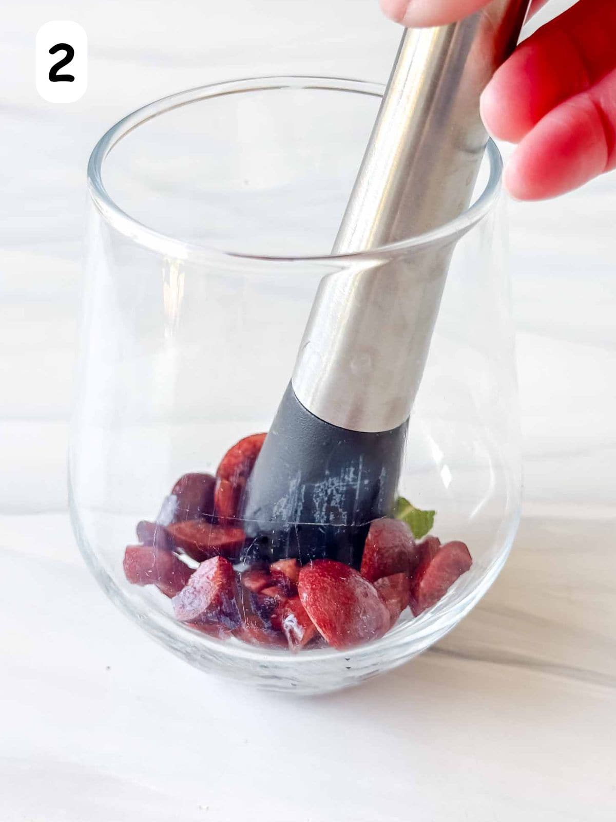 cherries and mint leaves being muddled in a glass with a muddler labelled number two.