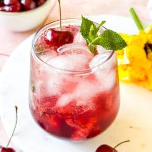 cherry mocktail in a glass garnished with mint leaves and a cherry.