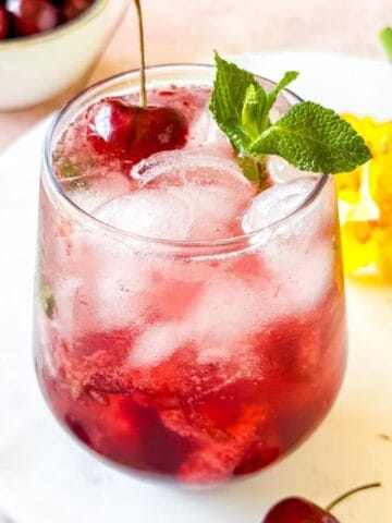 cherry mocktail in a glass garnished with mint leaves and a cherry.