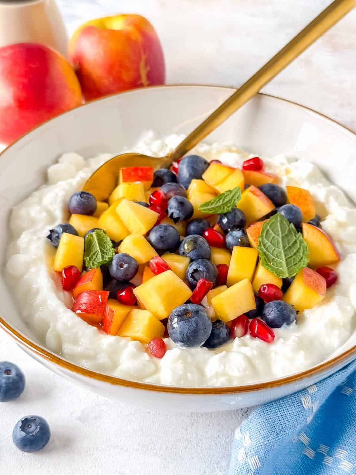 cottage cheese fruit salad in a white bowl with a spoon in it.