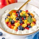 cottage cheese fruit salad in a white bowl garnished with mint leaves.