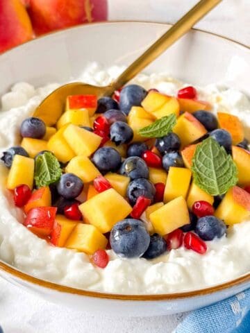 cottage cheese fruit salad in a white bowl garnished with mint leaves.