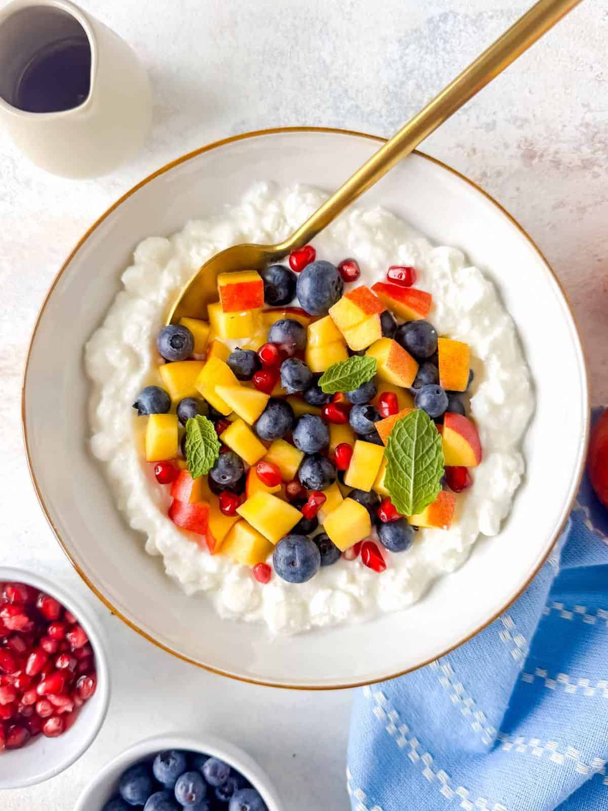cottage cheese fruit salad in a white bowl next to a small jug of maple syrup.