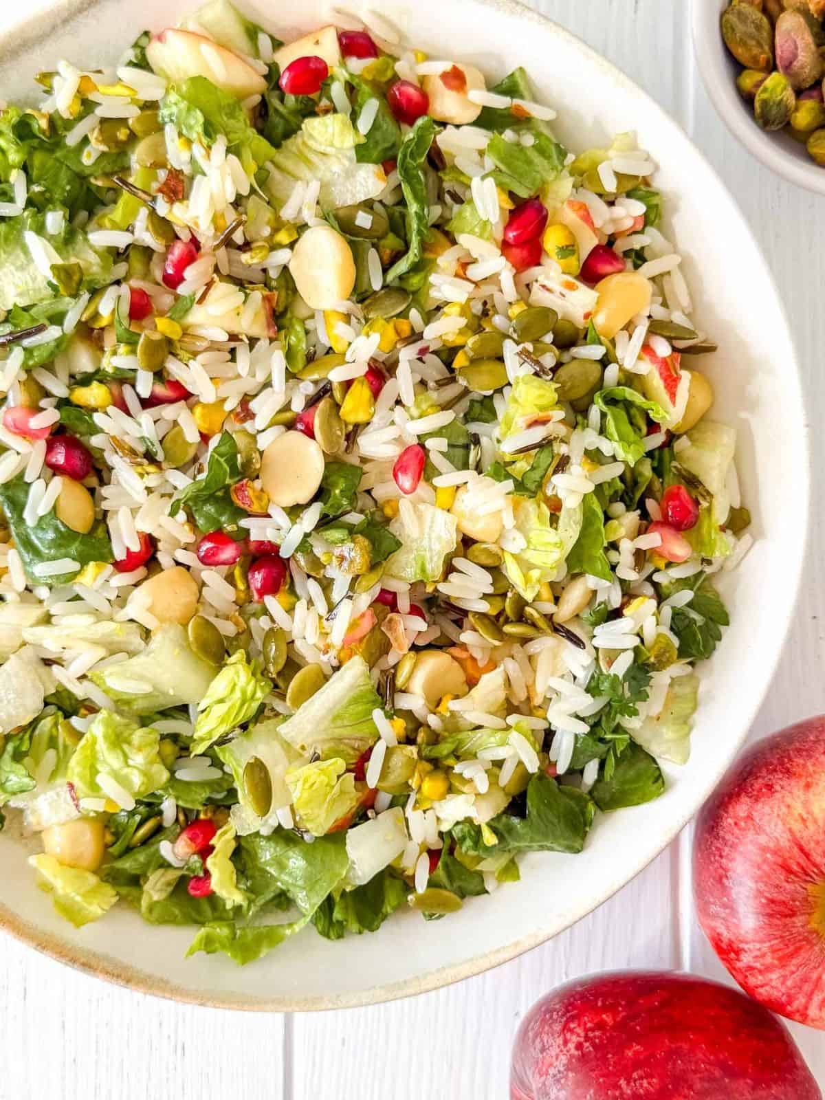 fruit and nut salad with rice in a white bowl next to red apples.