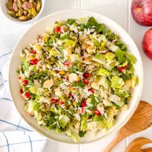 fruit and nut salad in a bowl next to red apples and pistachios.