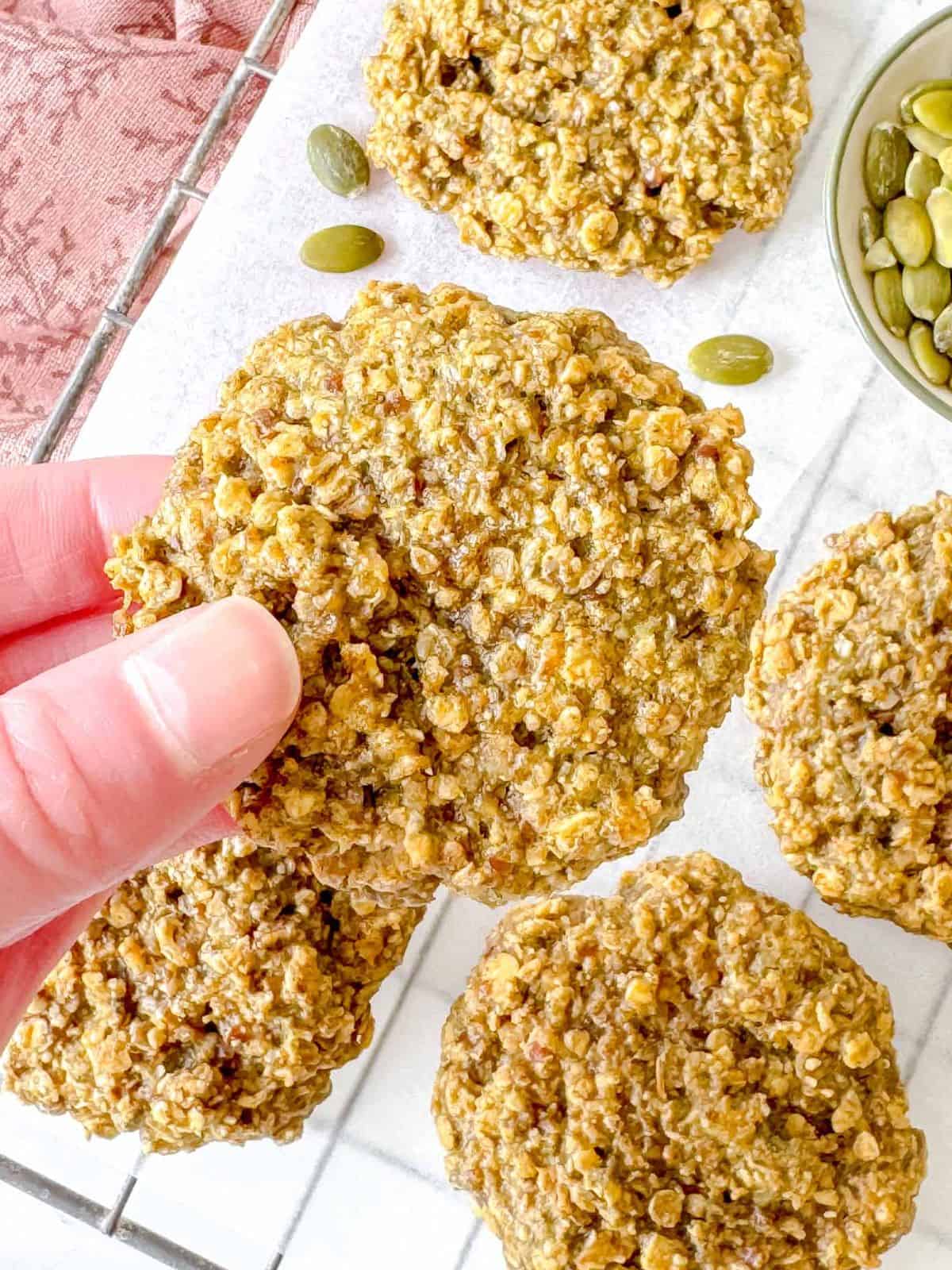 a pumpkin seed butter cookie being held above other cookies.
