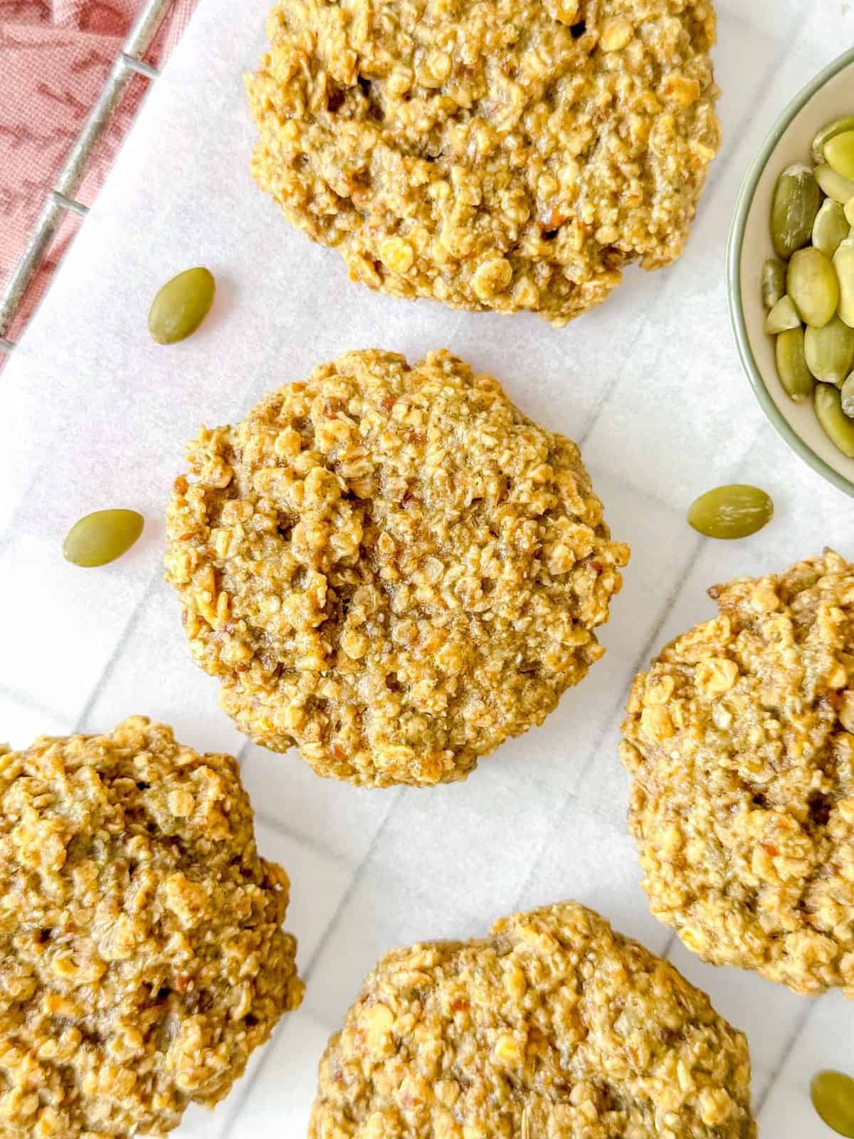 pumpkin seed butter cookies on parchment paper next to a small bowl of pumpkin seeds.