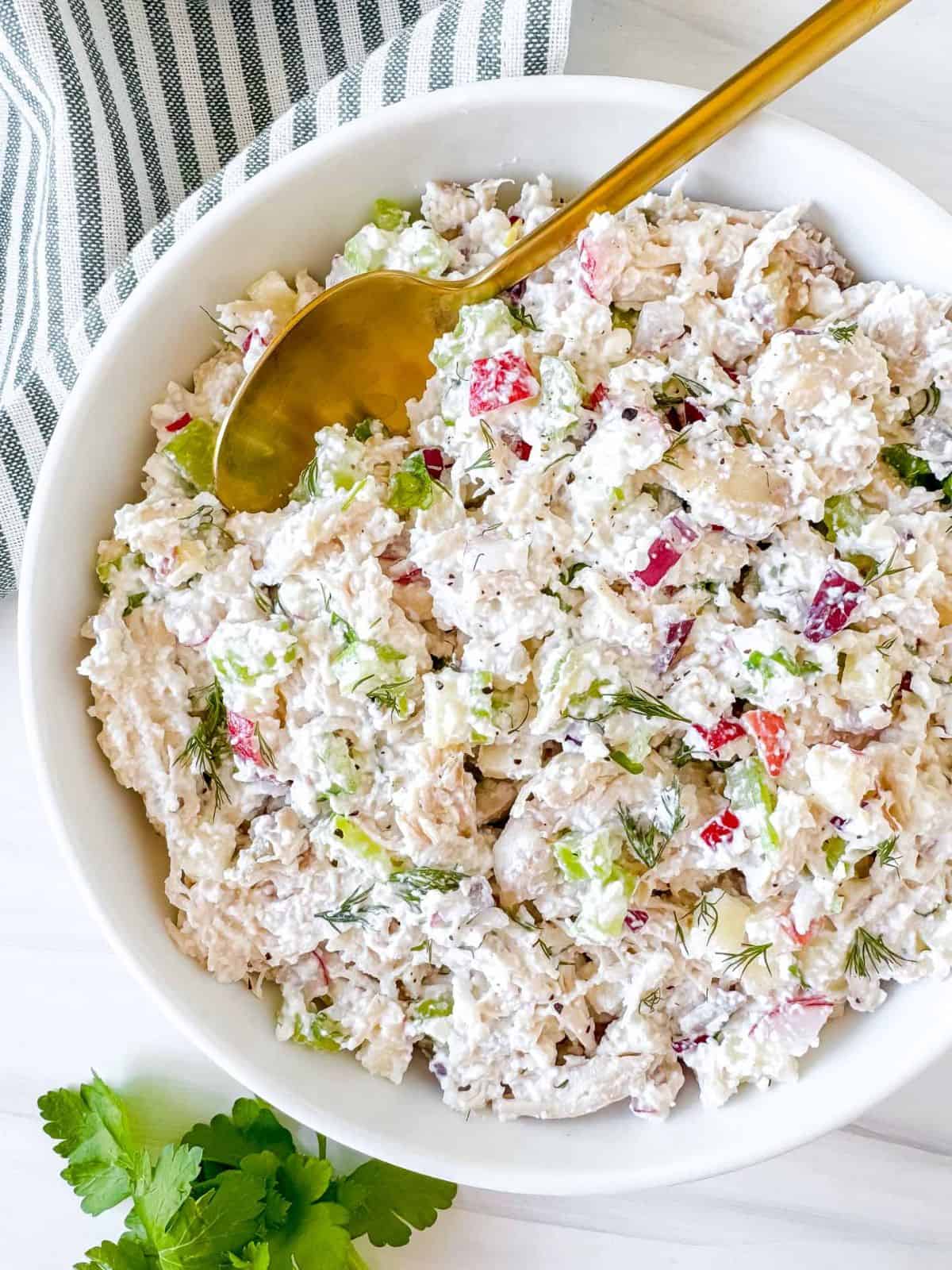 cottage cheese chicken salad in a white bowl with a gold spoon in it next to parsley leaves.
