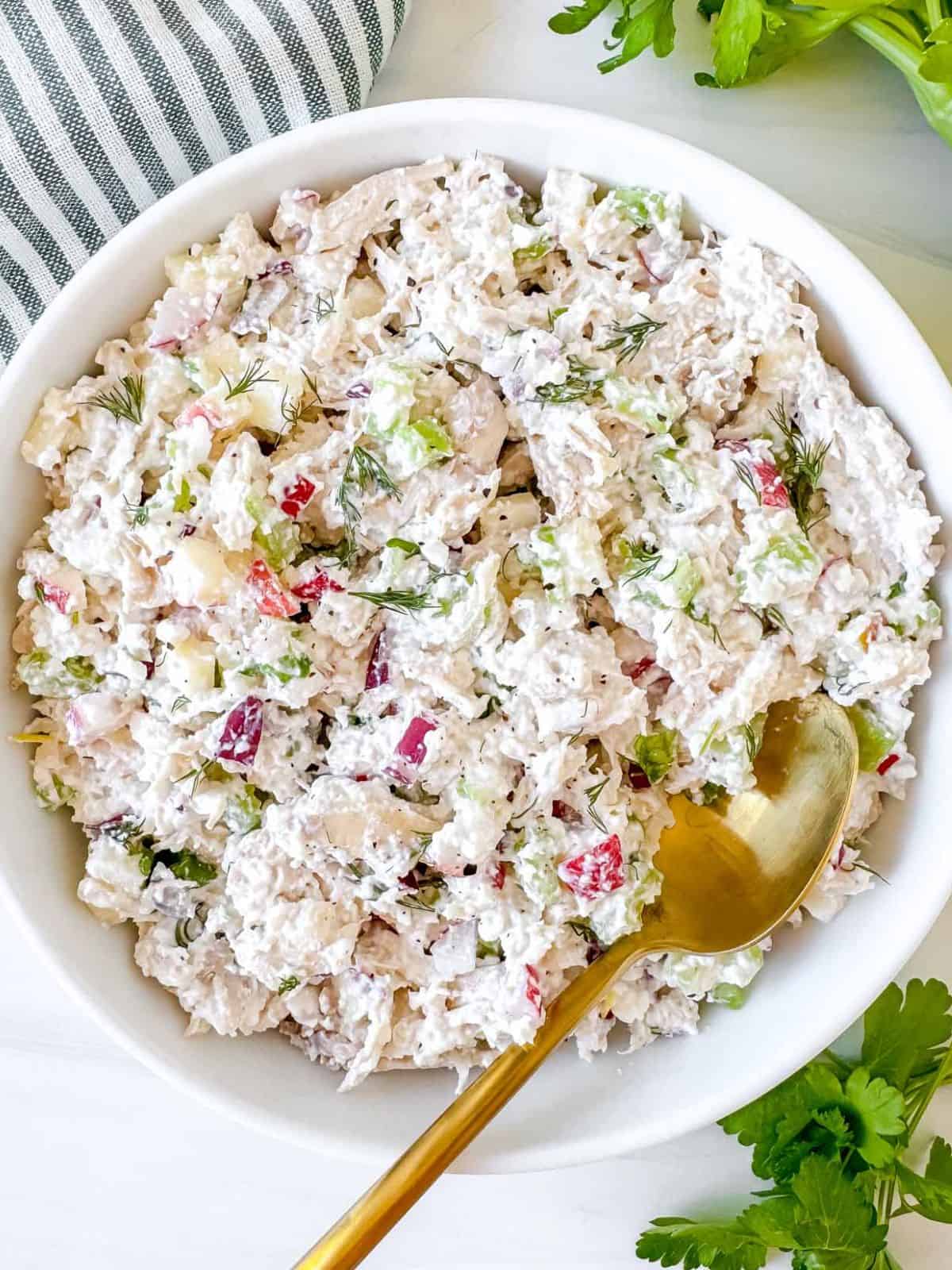 cottage cheese chicken salad in a white bowl next to celery and a striped cloth.