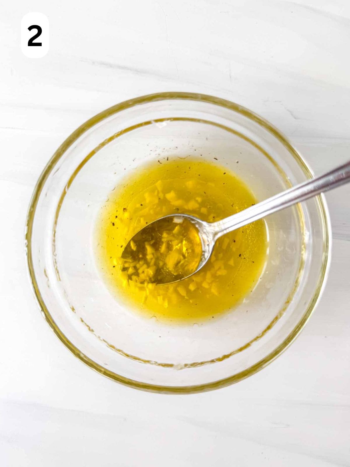 olive oil dressing in a glass bowl with a spoon in it labelled number two.