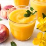 frozen peach slush without wine next to fresh peaches, mint leaves and yellow flowers.
