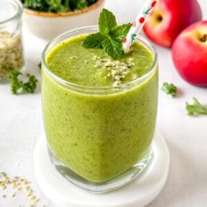 low histamine smoothie in a glass next to leafy greens, fruit and hemp seeds.