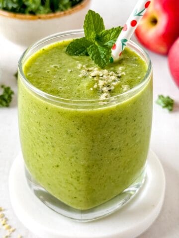 low histamine smoothie in a glass next to leafy greens, fruit and hemp seeds.