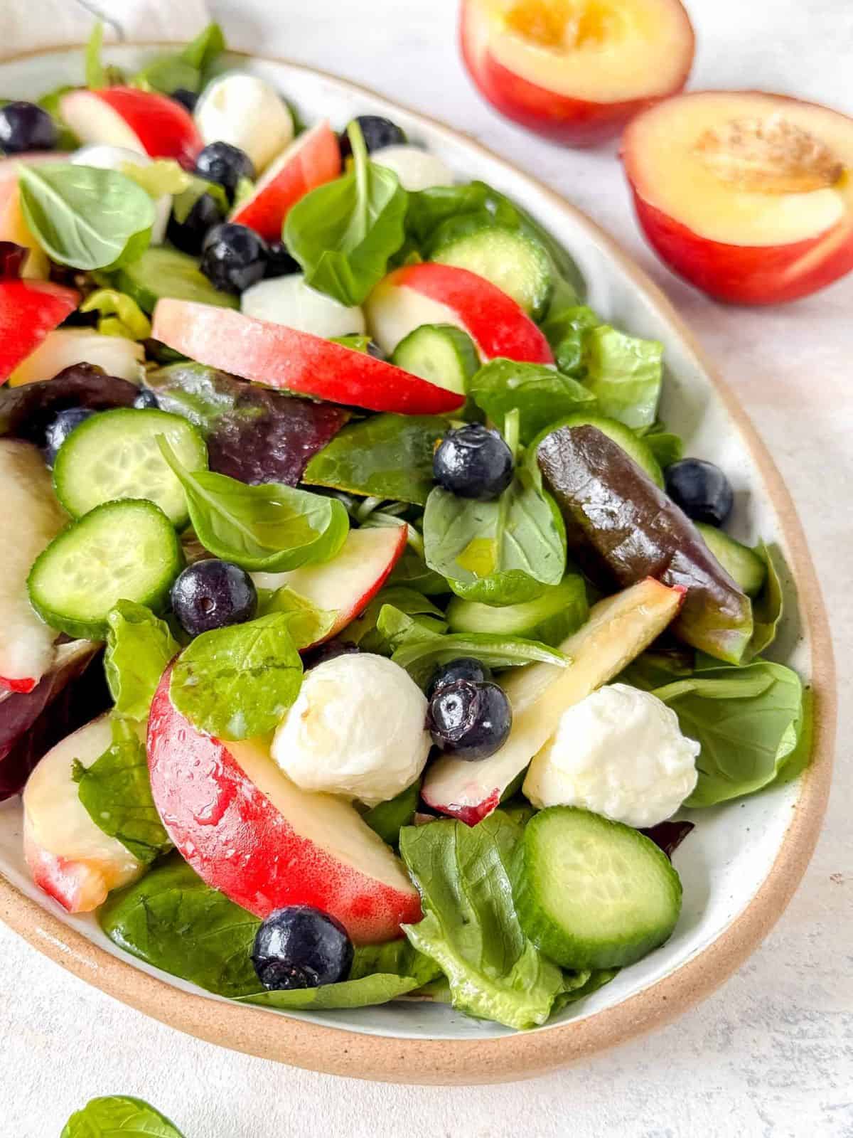 nectarine salad with mozzarella and cucumber on a plate next to fresh nectarines.