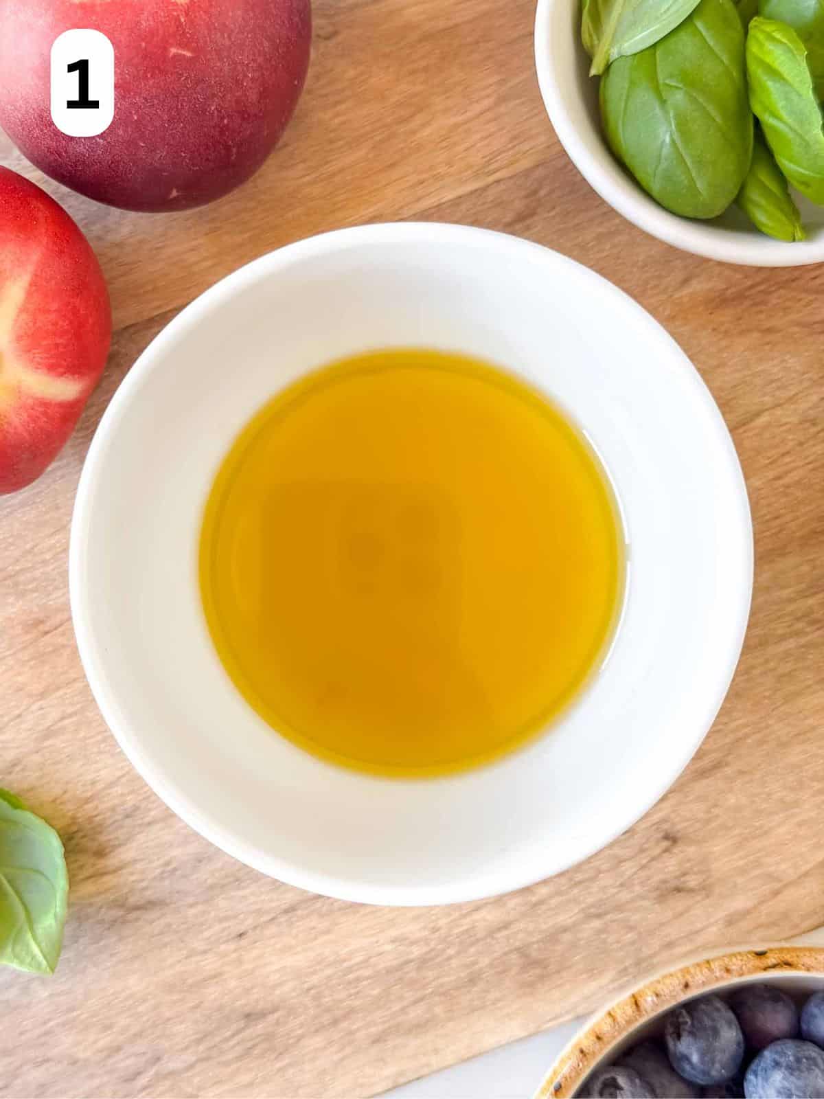 olive oil and apple cider vinegar dressing in a white bowl surrounded by nectarines, basil leaves and blueberries labelled number one.