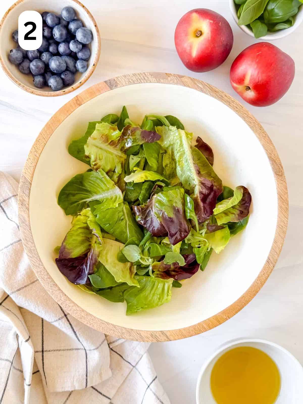 lettuce leaves in a large bowl next to nectarines, blueberries and basil leaves labelled number two.