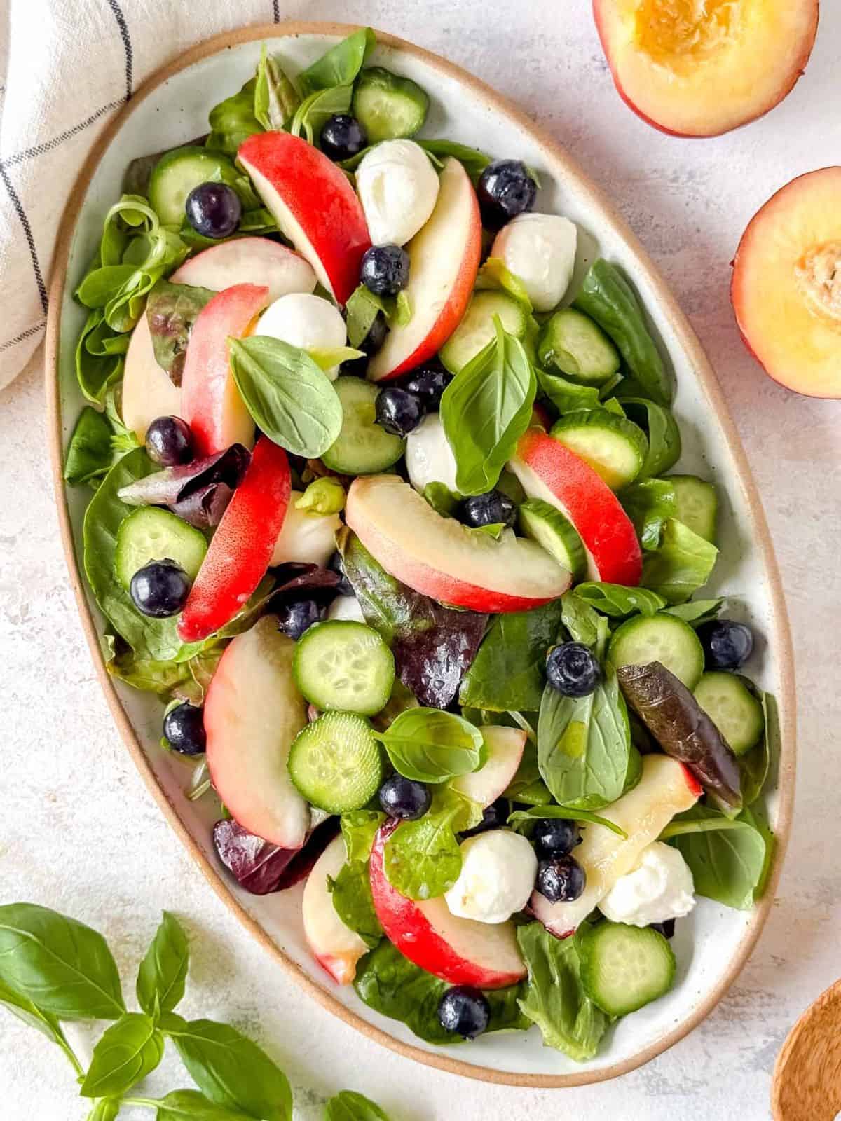 nectarine salad with mozzarella and basil on a plate next to fresh nectarines and basil leaves.