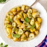 no mayo potato salad with dill and mint in a white bowl with a spoon.