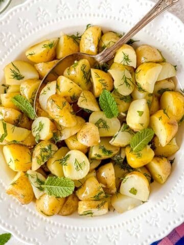 no mayo potato salad with dill and mint in a white bowl with a spoon.