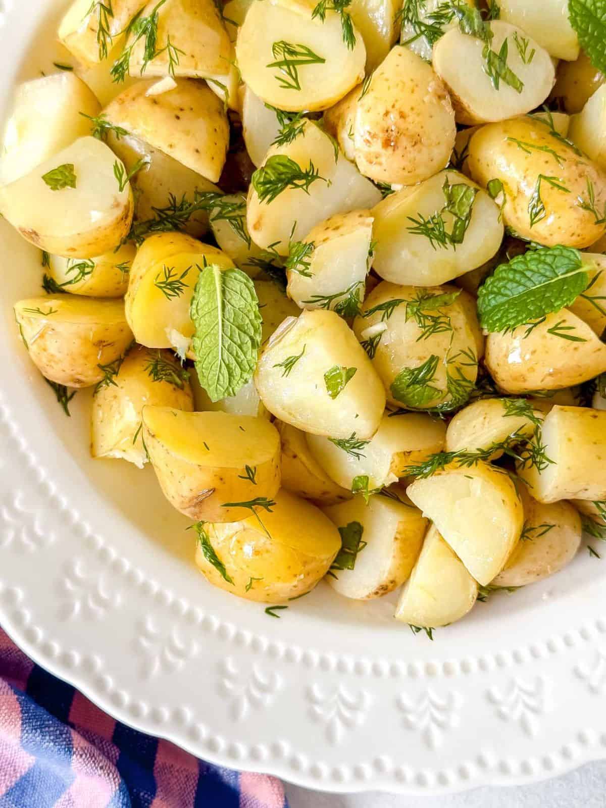 new potato salad without mayo in a white bowl garnished with mint leaves.